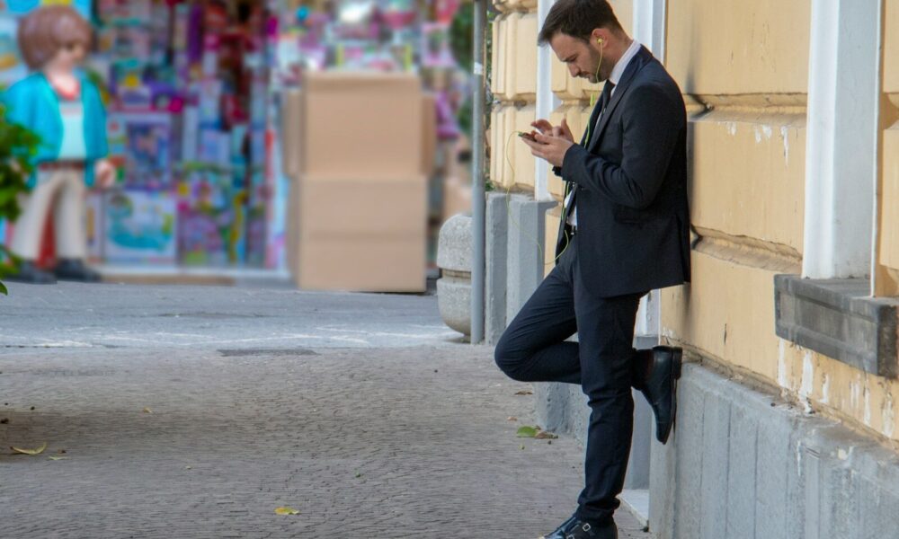 man holding his phone while leaning on building