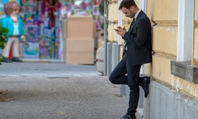 man holding his phone while leaning on building