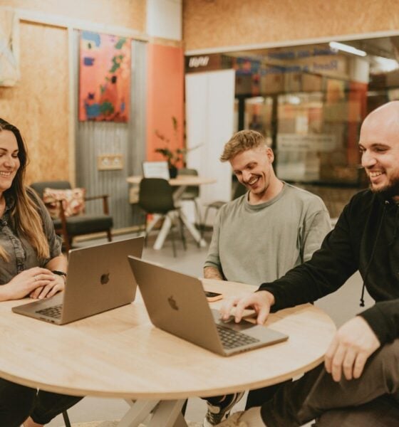 Three people collaborate around a table with laptops.