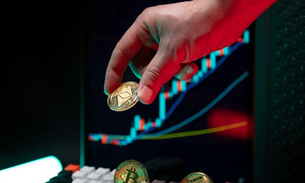 Hand holding ethereum with crypto graphs in background.