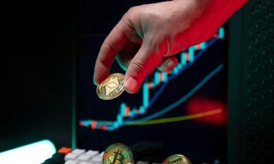 Hand holding ethereum with crypto graphs in background.