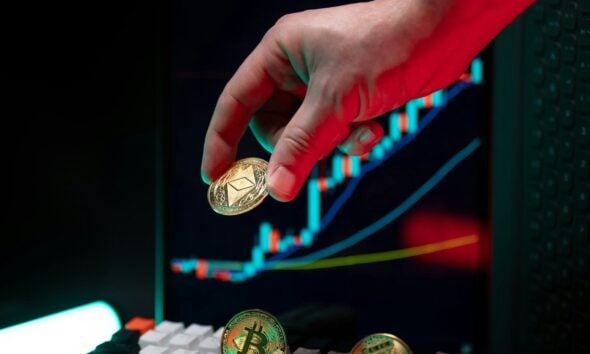 Hand holding ethereum with crypto graphs in background.