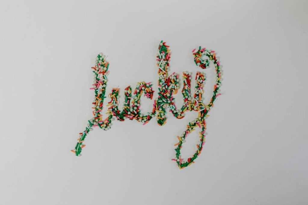 The word 'lucky' spelled out in colorful candy sprinkles on a white background, conveying a cheerful mood.