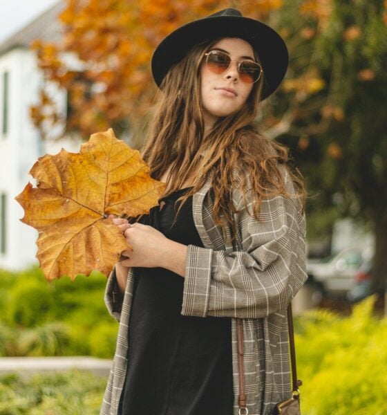 a woman in a hat and sunglasses holding a leaf