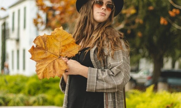 a woman in a hat and sunglasses holding a leaf