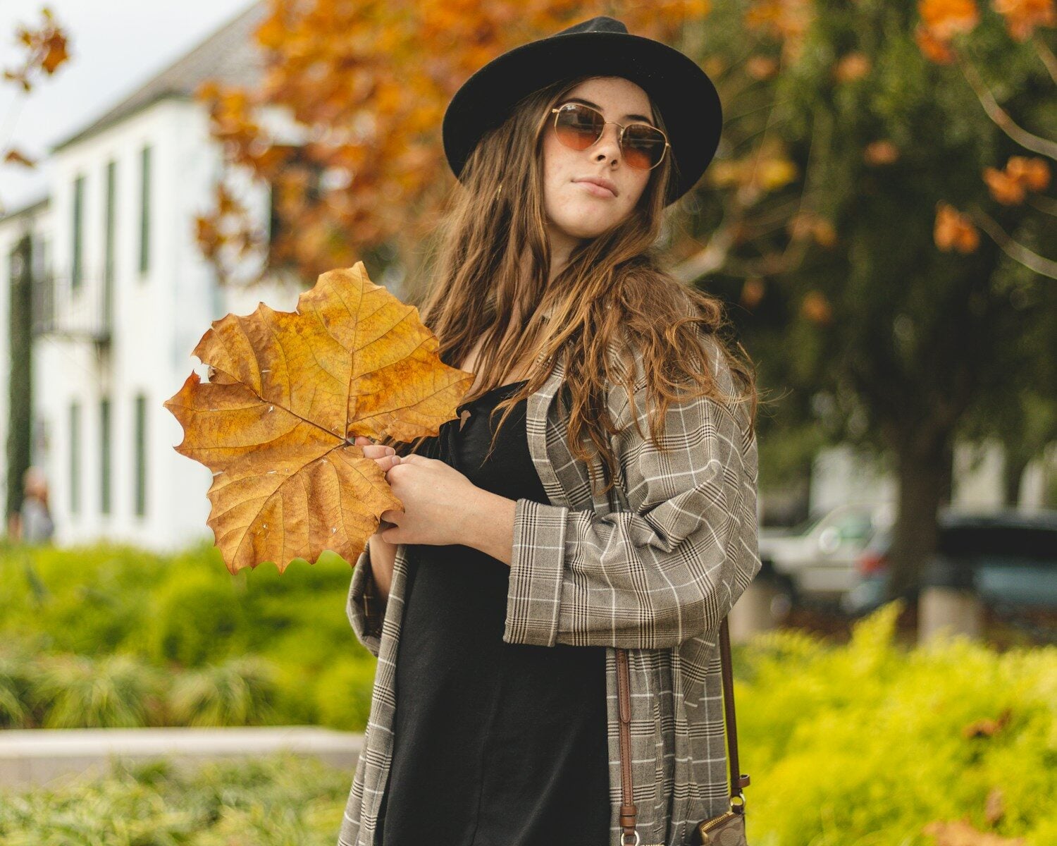 a woman in a hat and sunglasses holding a leaf