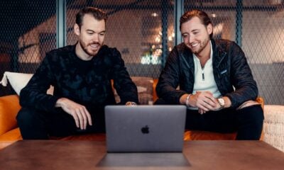 two men sitting at a table looking at a laptop