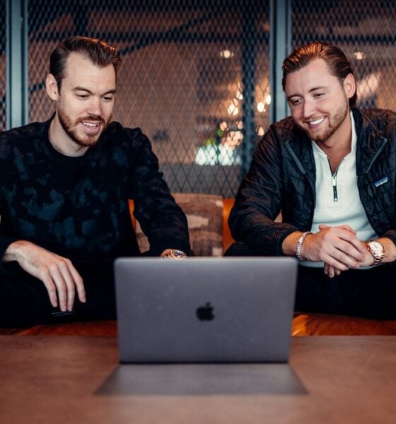 two men sitting at a table looking at a laptop