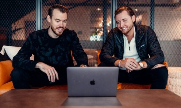 two men sitting at a table looking at a laptop