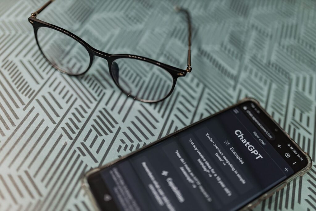 VetClaims.ai Review: Features, Pros, Cons, and Pricing 28 Eyeglasses next to a smartphone displaying the ChatGPT AI app on a patterned surface.
