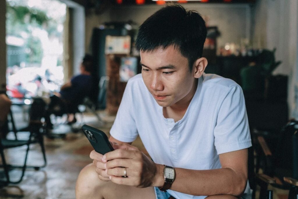 Casually dressed young man engaged with his smartphone, seated indoors.