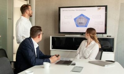 Three people in a meeting room looking at a presentation.