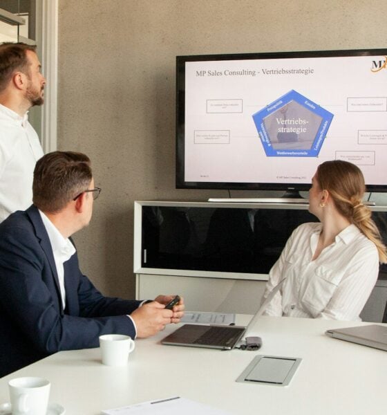 Three people in a meeting room looking at a presentation.