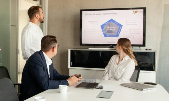 Three people in a meeting room looking at a presentation.