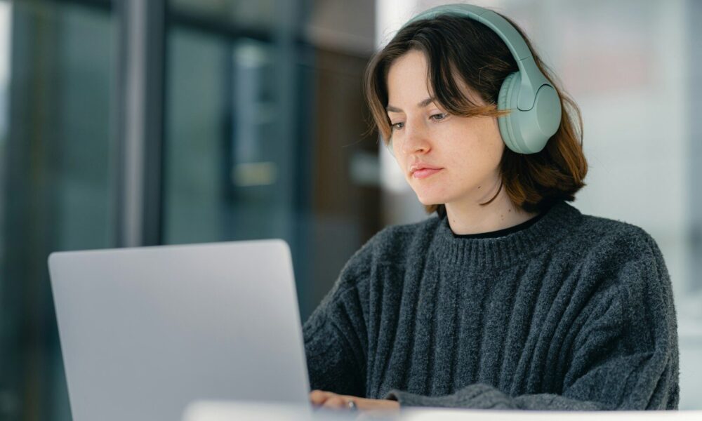 A woman sitting at a table with a laptop wearing headphones