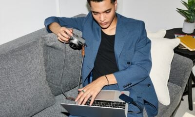 Young man using laptop and camera on sofa.