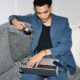Young man using laptop and camera on sofa.