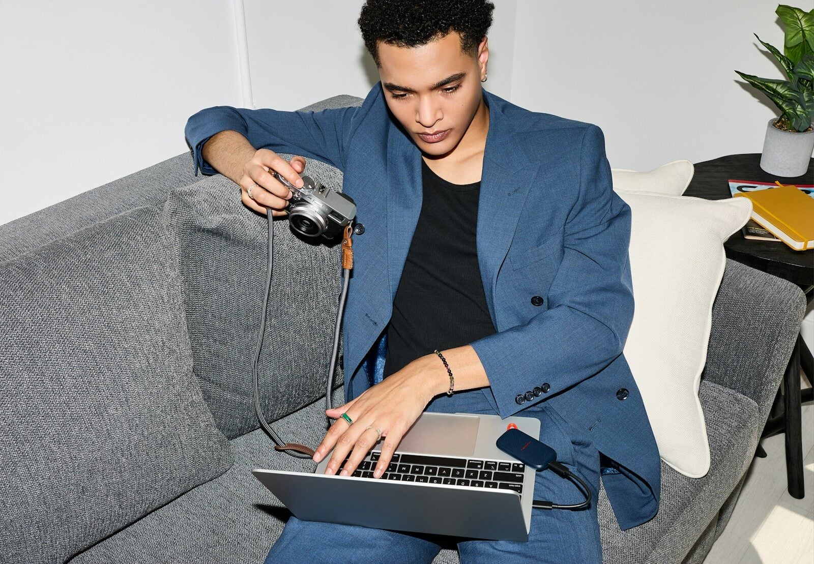 Young man using laptop and camera on sofa.