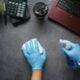 Hands in blue gloves cleaning a dark desk with a spray bottle and cloth