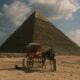 A donkey pulls a carriage in front of a pyramid.
