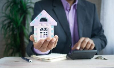 man holding model house at desk with calculator
