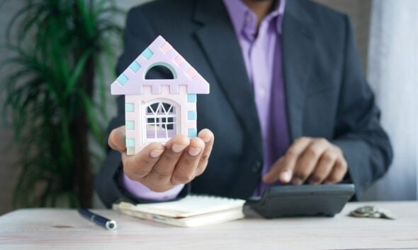 man holding model house at desk with calculator