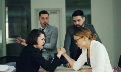 Two women arm wrestling with men watching