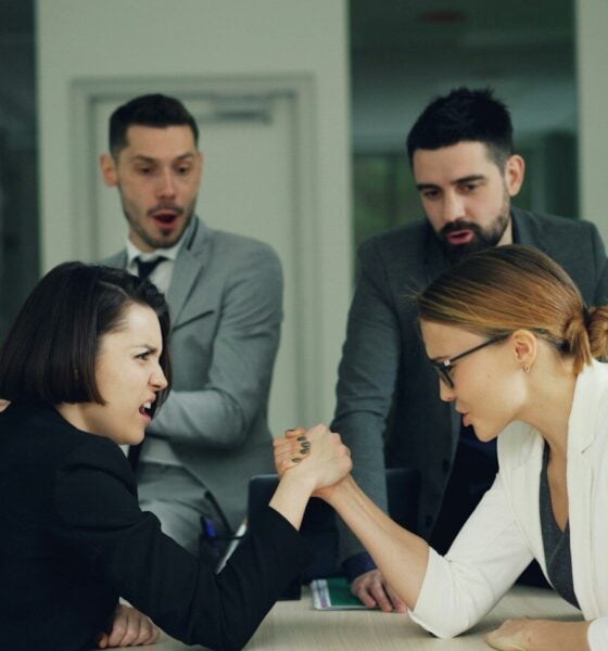 Two women arm wrestling with men watching
