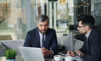 two men sitting at a table working on a laptop