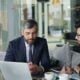 two men sitting at a table working on a laptop