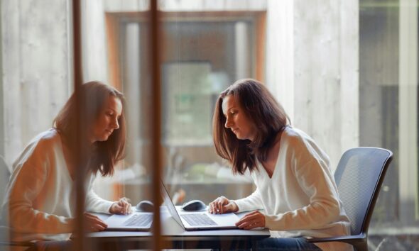 two women sitting at a table working on a laptop
