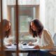 two women sitting at a table working on a laptop