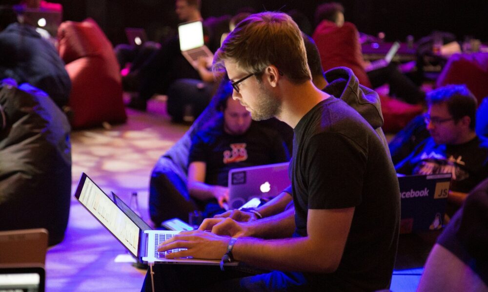 A man in glasses typing on a laptop in a dimly lit workspace