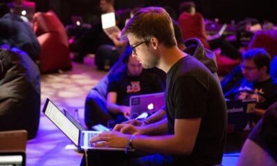 A man in glasses typing on a laptop in a dimly lit workspace