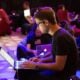 A man in glasses typing on a laptop in a dimly lit workspace