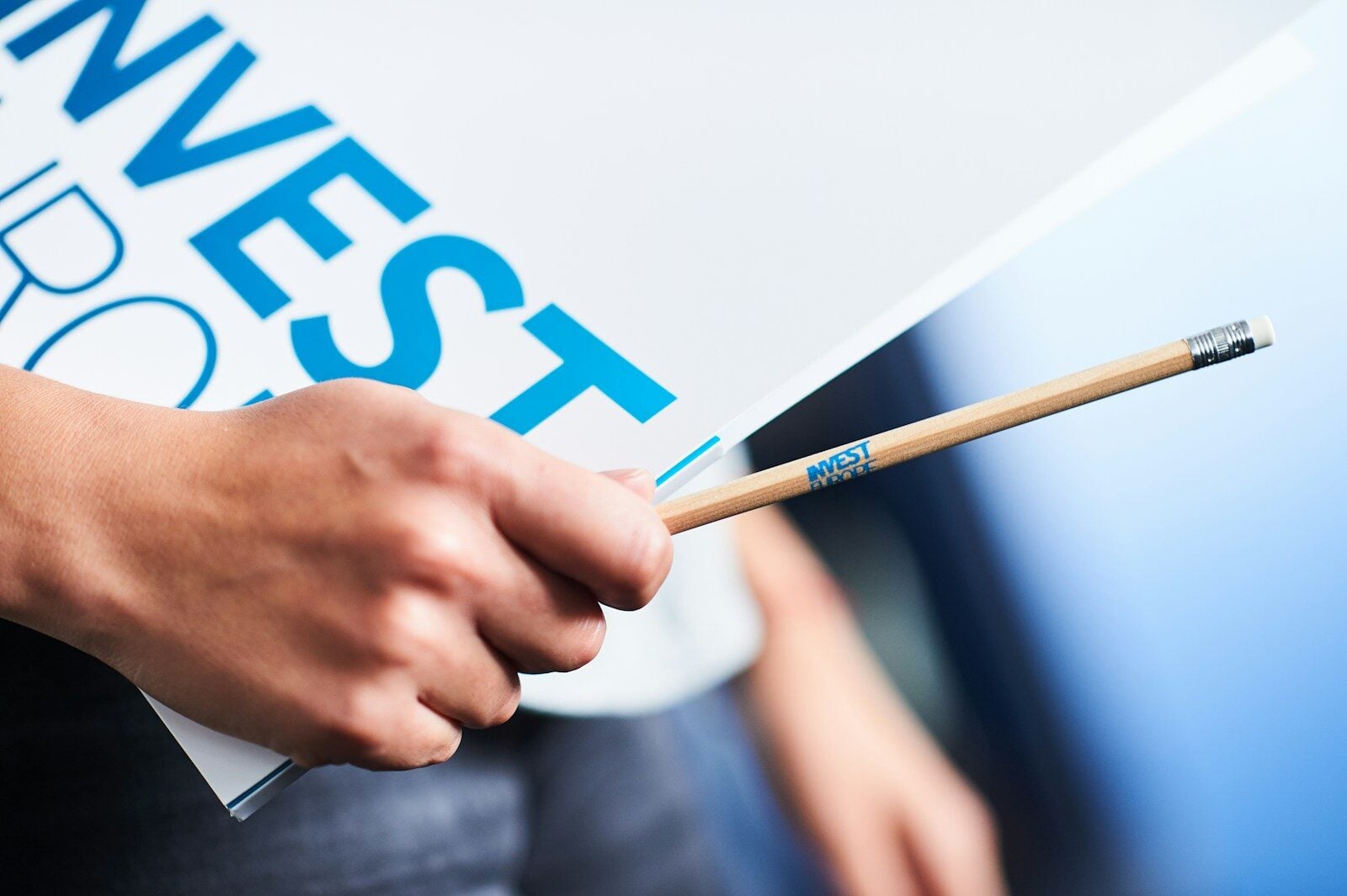 Hand holding "invest" sign and pencil