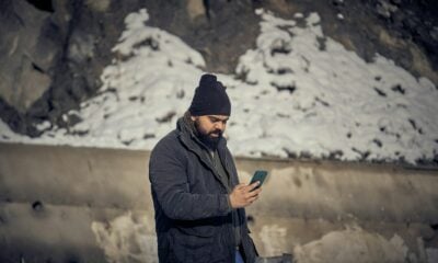 A man with a beard and black beanie using a smartphone outdoors