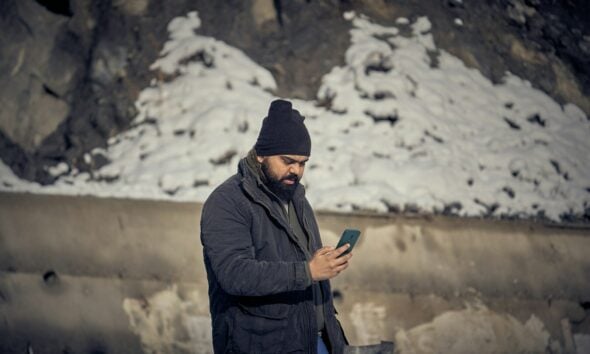 A man with a beard and black beanie using a smartphone outdoors