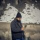 A man with a beard and black beanie using a smartphone outdoors
