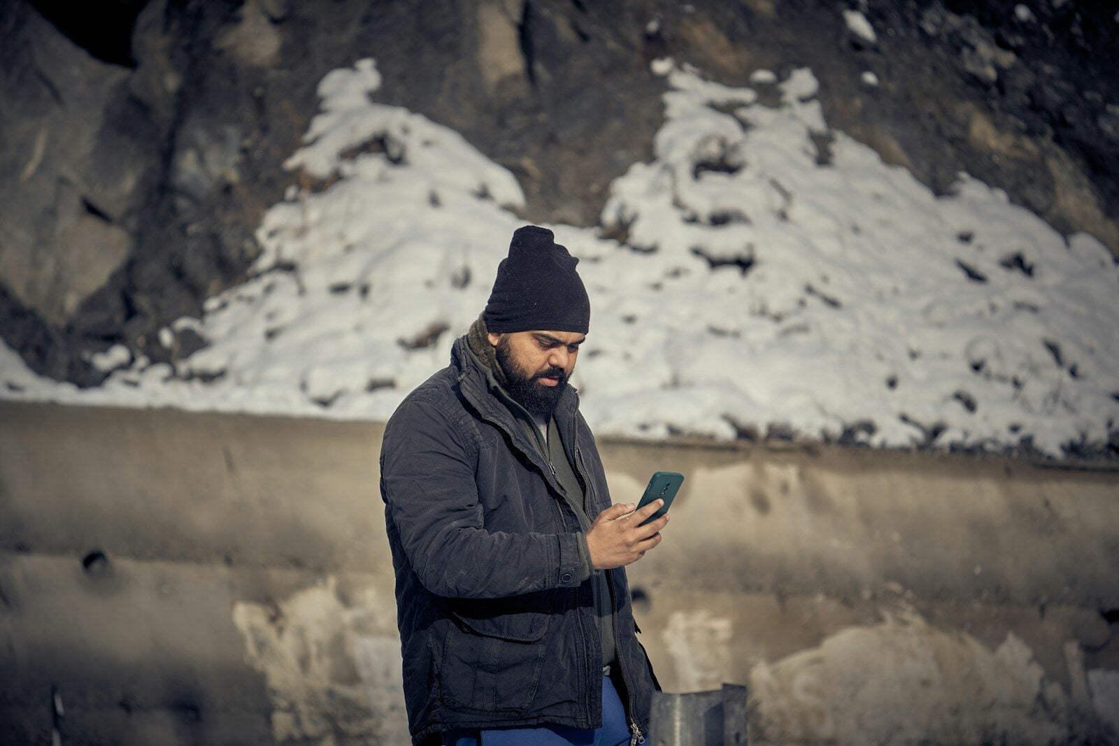 A man with a beard and black beanie using a smartphone outdoors
