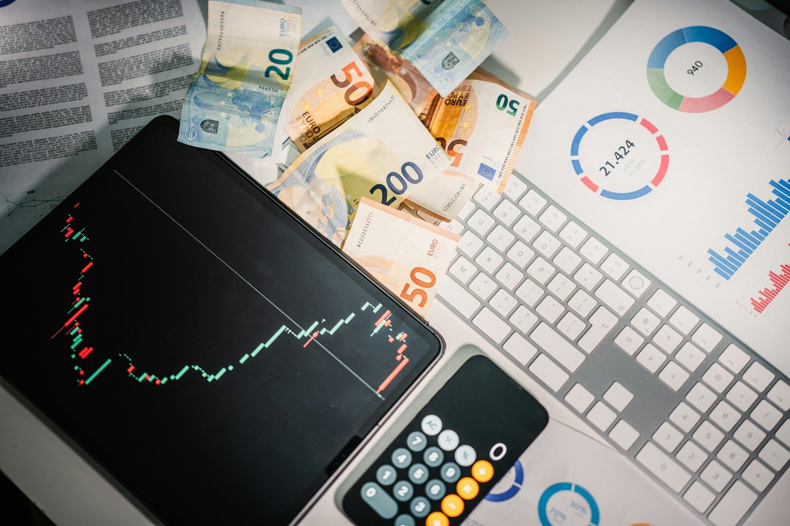 Euro banknotes, a tablet with a stock chart, and financial reports on a desk