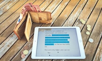 Wallet, tablet with financial data, and coins on wooden table