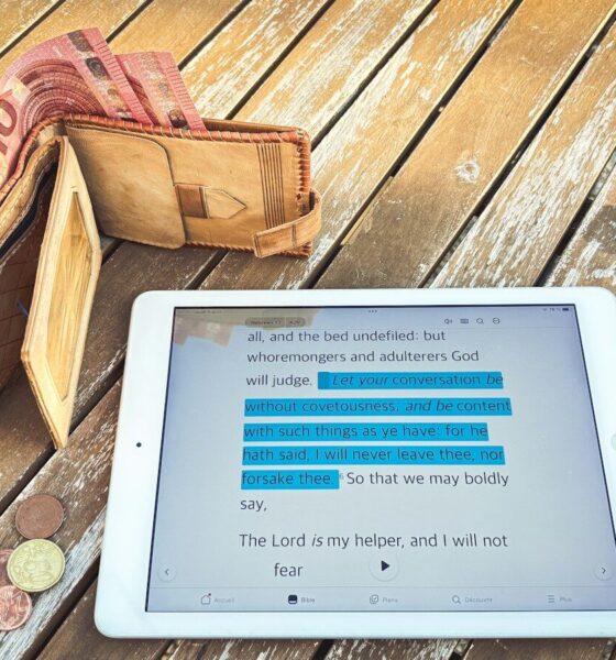 Wallet, tablet with financial data, and coins on wooden table