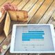 Wallet, tablet with financial data, and coins on wooden table