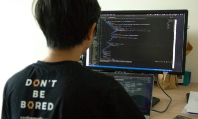 man in black shirt using laptop computer and flat screen monitor