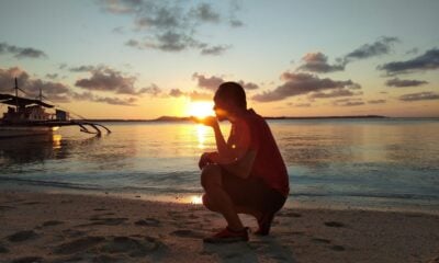 woman in red dress sitting on beach during sunset