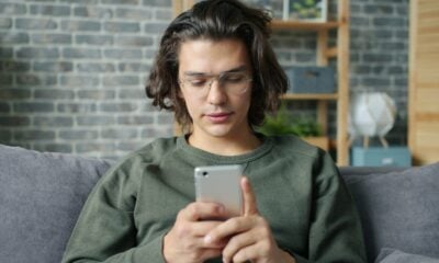 Young man with glasses using a smartphone on couch