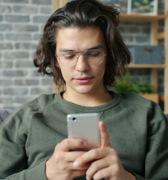 Young man with glasses using a smartphone on couch