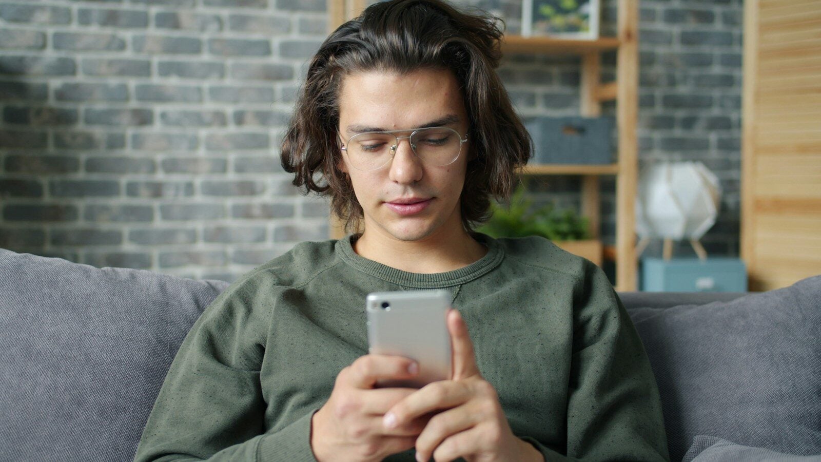 Young man with glasses using a smartphone on couch