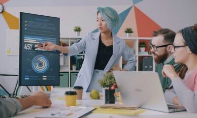 A woman with blue hair pointing at a digital chart during a team meeting